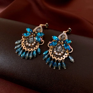 Macro detail of bohemian fringe earrings with peacock blue crystals and gold plating