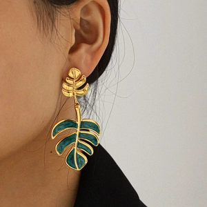 Golden monstera leaf earrings with dark green enamel finish on female model