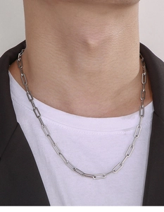 Close-up of a silver rectangular link paperclip chain necklace worn on a neck