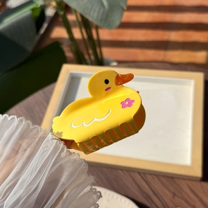 Pinza per capelli a forma di anatra gialla con fiori rosa su superficie di legno soleggiata