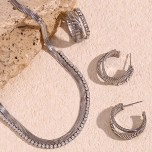 Detailed set of silver jewelry with herringbone texture and rhinestones on stone background