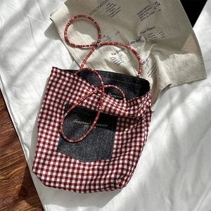 Detail of red checkered tote bag with denim pocket and woven rope handle in home setting