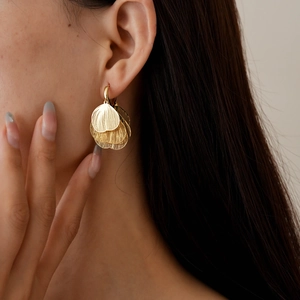 Close-up of golden hollow heart-petal layered earrings worn by a model
