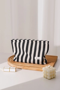 Close-up of striped canvas makeup bag with lipstick and candle on a wooden tray