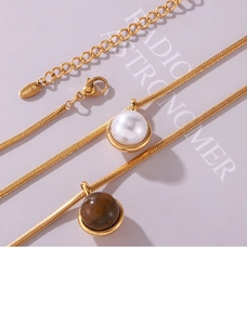 Detail of gold snake chain necklace featuring tiger eye stone and white shell pearl pendants