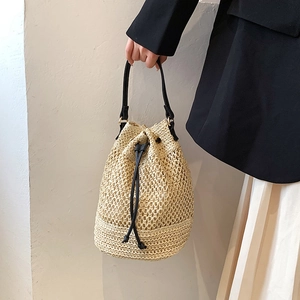 Handmade beige woven straw bucket bag with black drawstring straps for beach travel