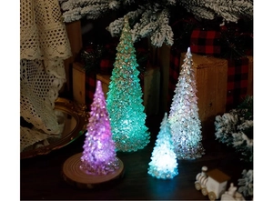 Close-up of four colorful glowing acrylic Christmas trees on a wooden tray with pine needles