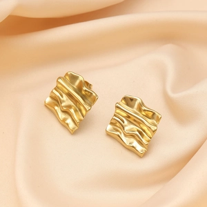 Macro shot of gold-plated wavy earrings on elegant beige silk fabric background