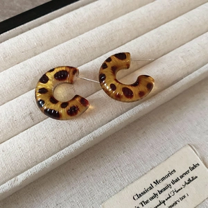 Detail of C-shaped leopard print resin hoop earrings on a velvet jewelry display tray