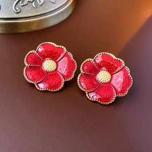 Macro shot of vintage red enamel flower earrings with golden edges on brown leather