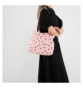 Detail of pink corduroy tote bag with red strawberry print shown on model shoulder