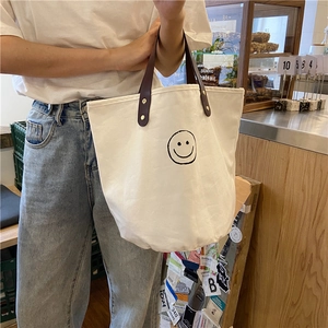 Detail of canvas tote bag with smiley face print and brown leather handle with gold rivets