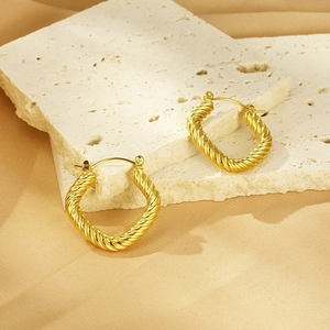 Close-up of gold geometric twisted square hoop earrings on a white mineral stone