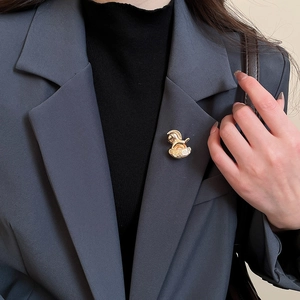 Détail d'une broche cheval à bascule dorée avec logo H sur un revers de veste gris