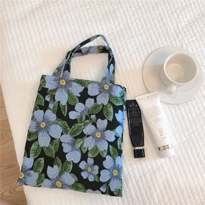 Close-up of blue floral jacquard fabric on a black cotton handbag with green leaves