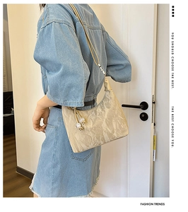 Detail of beige hobo bag with pleated satin texture and decorative beaded charm