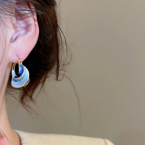 Macro view of gold twisted enamel hoop earrings with blue gradient on a female model