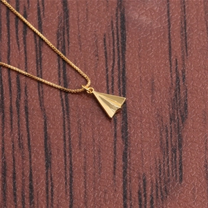Close-up of a gold paper plane pendant necklace on a dark textured background