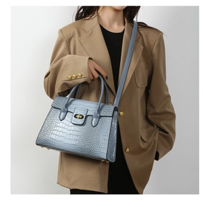 Detail of light blue crocodile pattern handbag with golden twist lock and shoulder strap