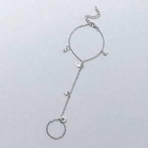 Silver star and moon pendant hand chain finger bracelet on a white textured surface