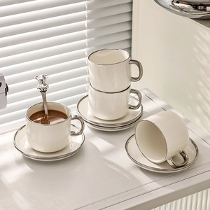 White ceramic coffee cup and saucer set with silver trim and bear handle spoon