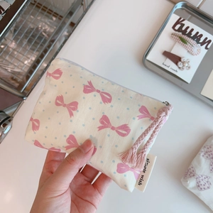 Handheld view of a floral cotton coin purse with pink bow prints and tassel zipper