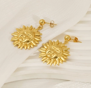 Macro shot of 18K gold plated sun face earrings with rays on a white fabric surface