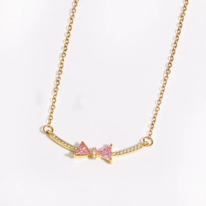 Close-up of golden necklace with pink zircon bow pendant on white background