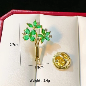 Elegant gold flower brooch with green gemstones and crystals in a jewelry box