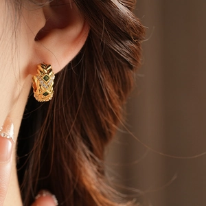 Close-up of vintage gold hoop earrings with green gemstone and quilted pattern on model