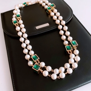 Detail of a vintage pearl necklace with a green gemstone pendant on black leather