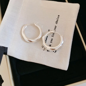 Close-up of silver irregular pleated hoop earrings on a minimalist white fabric bag