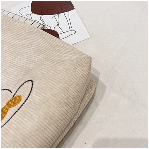 Detailed macro view of beige corduroy fabric texture with delicate embroidery details