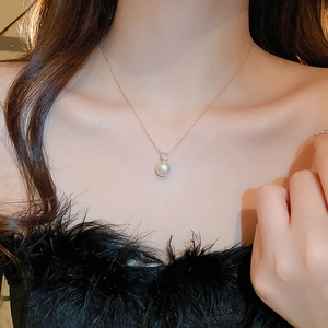 Detail shot of a lustrous white pearl pendant on a fine gold chain worn on the collarbone