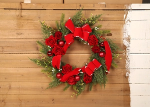 Detail of Christmas wreath with red roses, silk bows and ornaments on wooden background