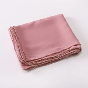 Close-up of pink silk scarf with decorative gold beads along the elegant edge