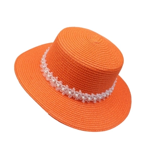 Detail of orange straw hat featuring elegant white lace trim and pearl accents