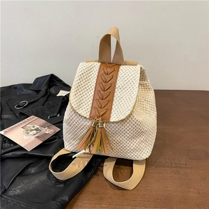 Straw backpack with tassel and brown leather accents on a rustic wooden table