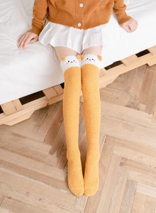 Close-up of yellow fuzzy over-knee socks featuring cute bear cartoon cuffs and soft plush fabric