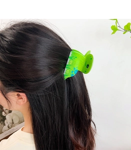 Detail view of a cute green dinosaur acrylic hair clip worn in a half-up hairstyle