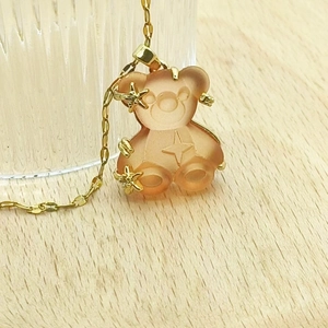 Macro detail of translucent orange resin bear pendant with gold stars on a gold chain
