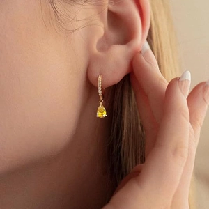 Close-up of elegant gold drop earring with yellow pear-cut zircon on model side profile