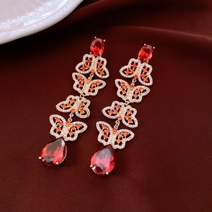 Close-up of golden butterfly earrings with red teardrop crystals on red velvet