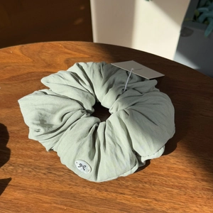 Light green linen scrunchie featuring a shell button with a black bow on a wooden surface