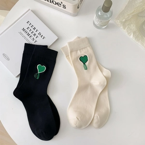 Dettaglio di calzini con ricamo a cuore verde e nappe coordinate in nero e bianco crema
