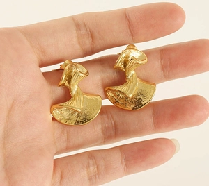 Macro detail of irregular hammered gold earrings with a twisted wave design and metallic texture