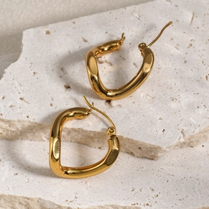 Chic irregular wavy gold hoop earrings displayed on a white textured stone surface