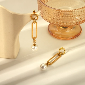 Elegant gold titanium steel earrings with white faux pearl drops on a minimalist display