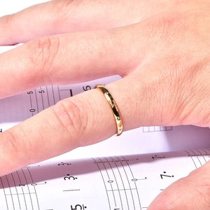 Close-up of gold 18k zircon teardrop ring on finger with elegant sheet music background