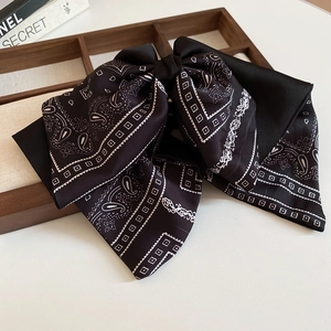 Close-up of black satin bow hair claw clip with white Paisley patterns and geometric dots
